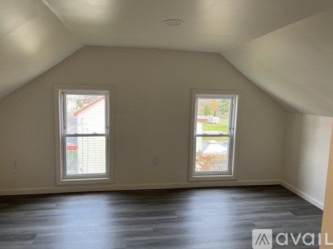A room with two windows and wooden floors is available for rent.
