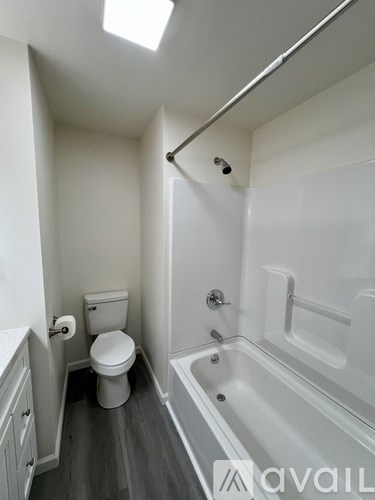 A white toilet sits in a small bathroom with a white bathtub.