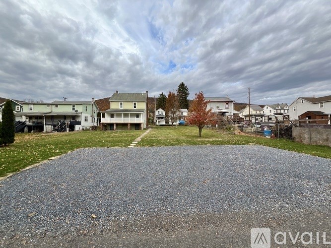 A gravel driveway leads to a house with a tree in the front yard.
