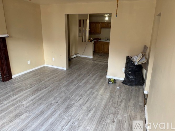 A room with wooden flooring and a wall with a black trash bag on the floor.