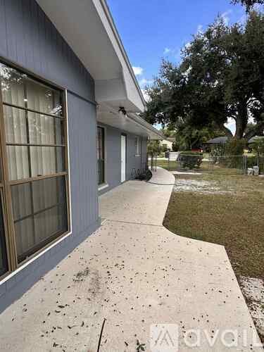 A concrete walkway leads to a house with a window on the left.