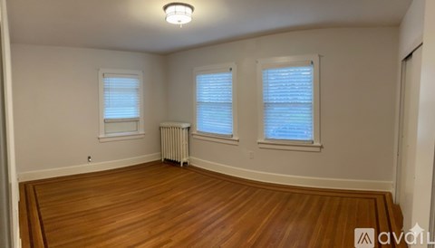 A room with wooden floors and two windows with blinds.