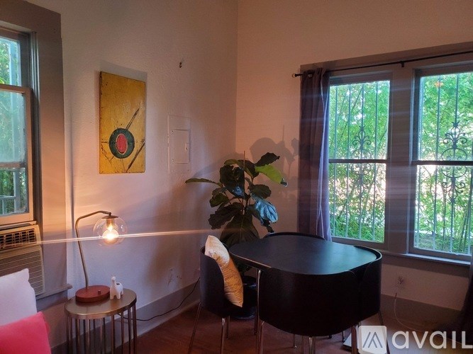 A room with a table, a lamp, a chair, and a painting on the wall.