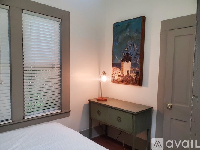 A bedroom with a bed, desk, and painting on the wall.