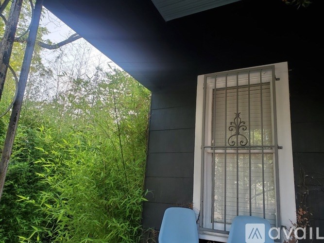 A window with bars and a blue chair is on the porch.