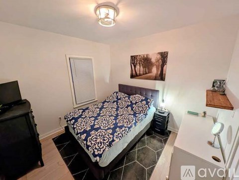 A bedroom with a bed, a television, and a painting on the wall.