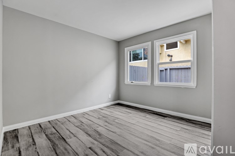 A room with wooden flooring and two windows.