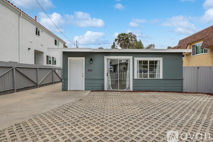 A house with a grey front and a white door is surrounded by a grey fence.