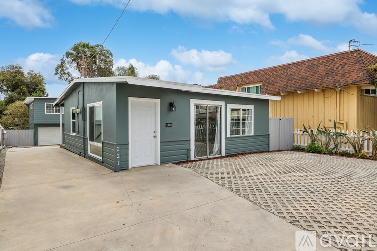 A grey house with a white door and windows is surrounded by a brick driveway.