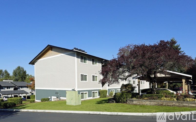 A modern two-story building with a grey and white exterior and a large tree in front.