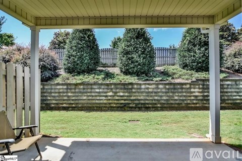 A covered patio area with a bench and a view of a garden and a fence.