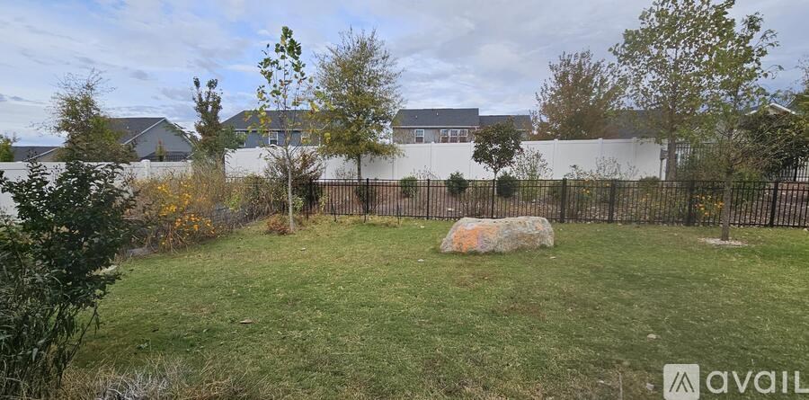 A grassy area with a large rock in the middle and a fence surrounding it.