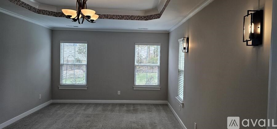 A room with a grey carpet and two windows.