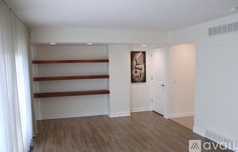 A room with wooden floors and white walls, featuring a white door and a picture on the wall.