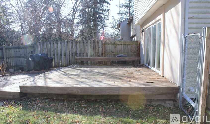 A wooden deck in a backyard with a fence and trees in the background.