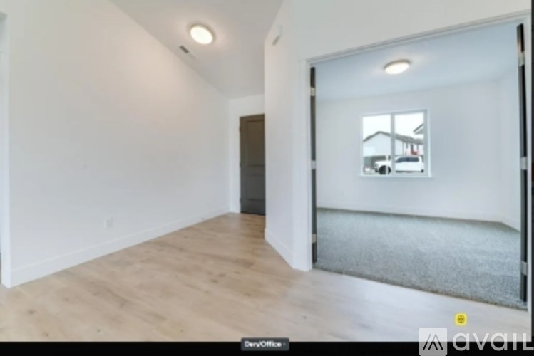 A room with wooden flooring and a white wall with a doorway leading to another room.