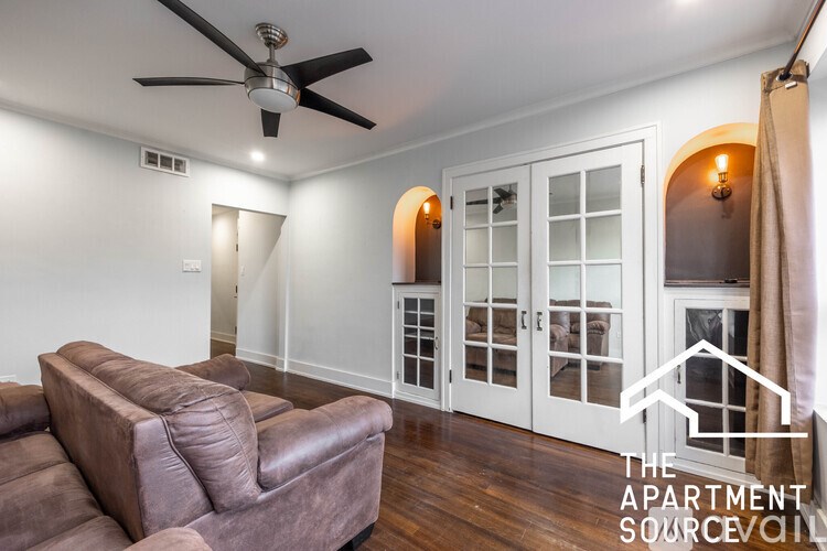 A living room with a brown leather couch and a ceiling fan.