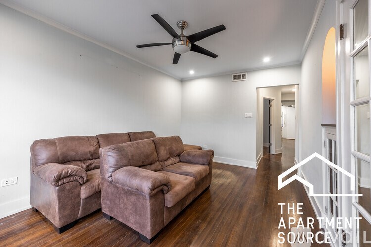 A living room with a brown leather couch and a ceiling fan.