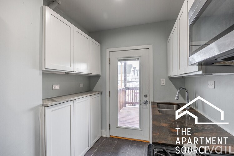 A small kitchen with white cabinets and a doorway leading to a balcony.