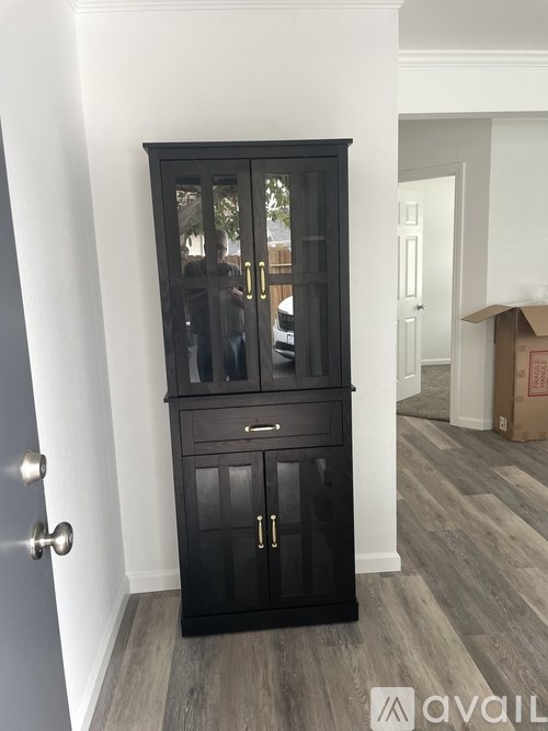 A black cabinet with glass doors and drawers is in a room with wooden flooring.