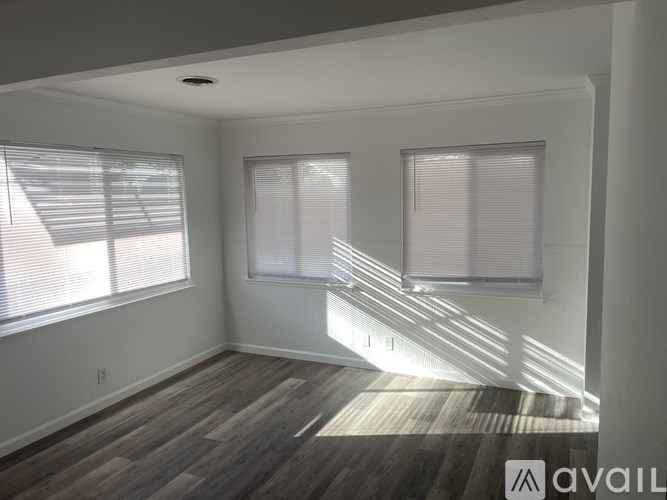 A room with wooden flooring and two windows with blinds.