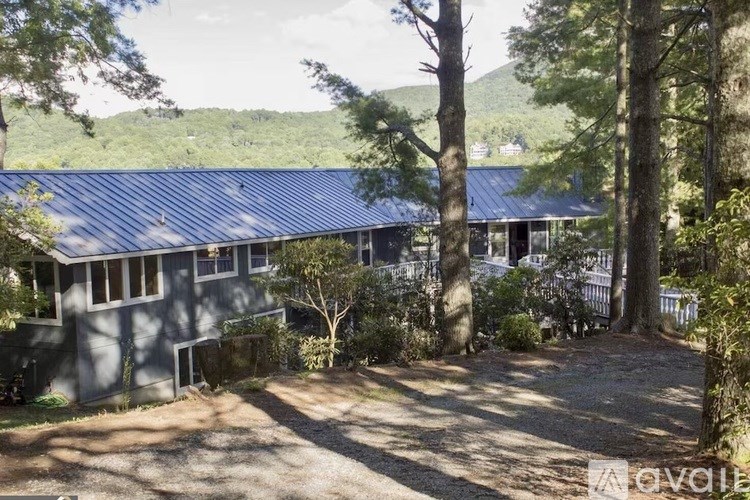 A house with a blue roof is surrounded by trees and has a gravel driveway.