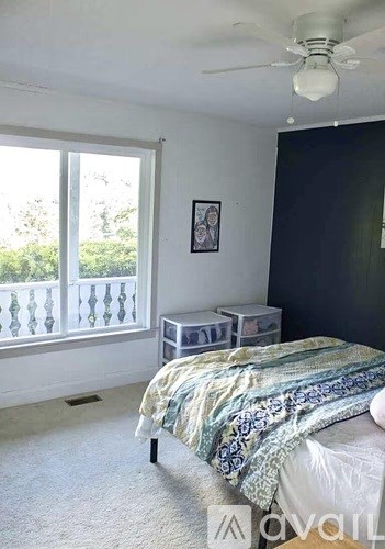 A bedroom with a bed, a ceiling fan, and a window with a view of trees.