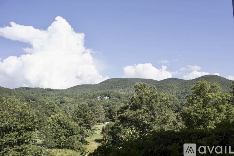 A landscape image of a mountainous area with trees and a cloud in the sky.