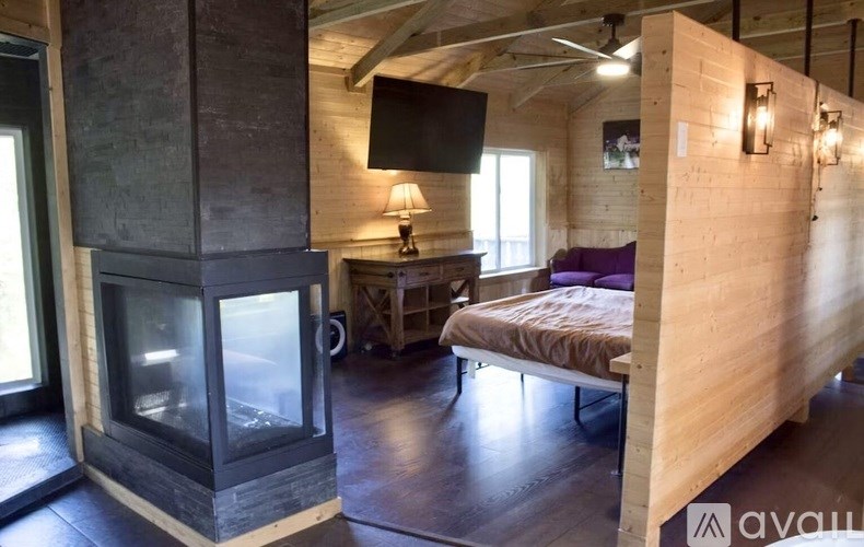 A modern bedroom with a wood-burning stove and a bed with a purple pillow.