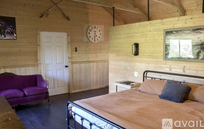 A bedroom with a bed, a couch, and a clock on the wall.