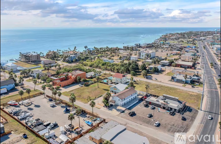 A small town with a parking lot in the foreground and the ocean in the background.
