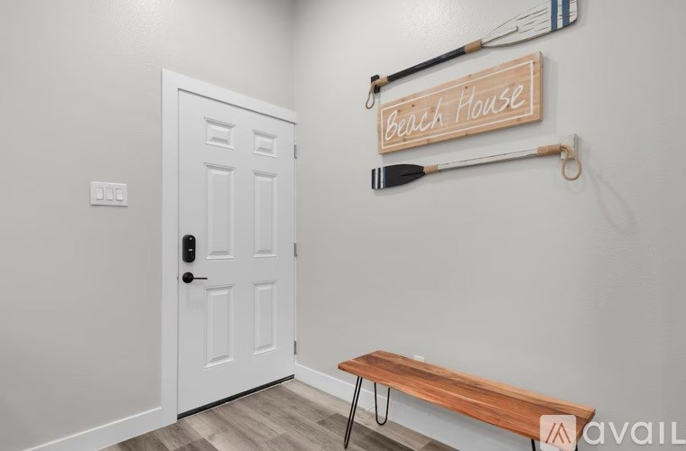 A white door with a black handle is in a room with a wooden bench and a sign that says "Beach House".