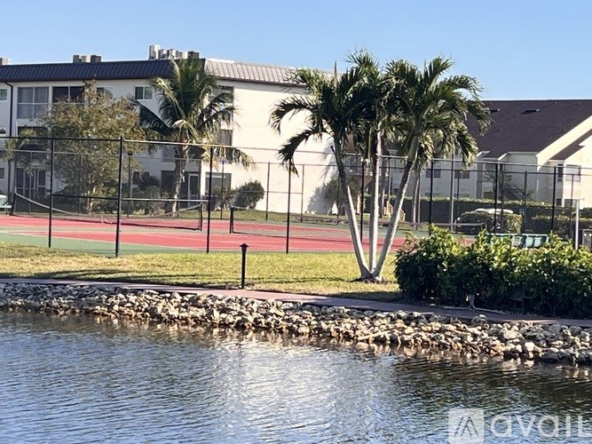 A body of water with rocks in front of a grassy area with a building in the background.