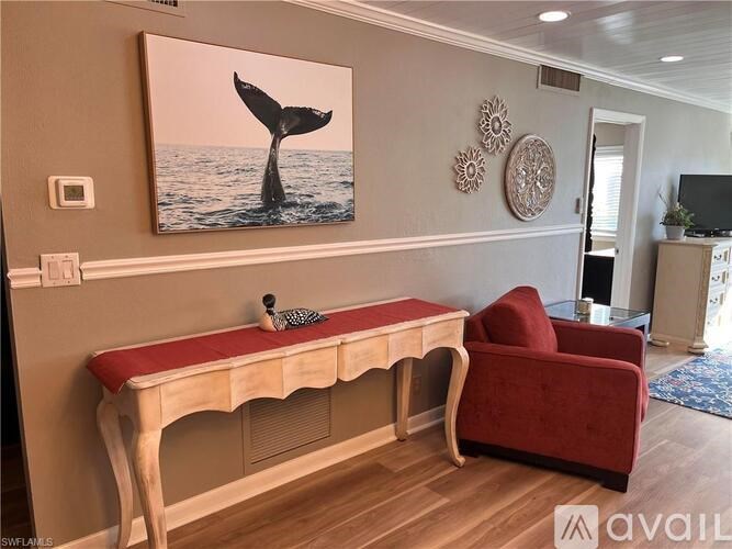 A whale tail painting hangs on a wall above a wooden desk with a red cushion.