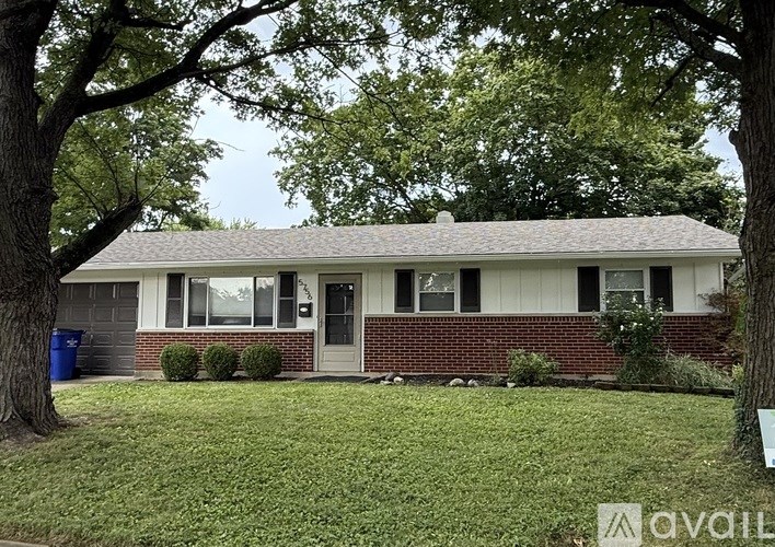 A house with a white door and windows is surrounded by greenery.