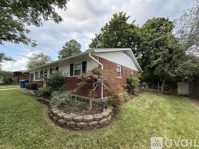 A house with a red brick exterior and a white roof is surrounded by a grassy area and trees.