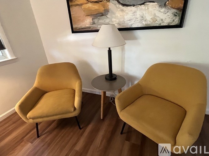 Two yellow chairs are placed in a room with a table and a painting on the wall.