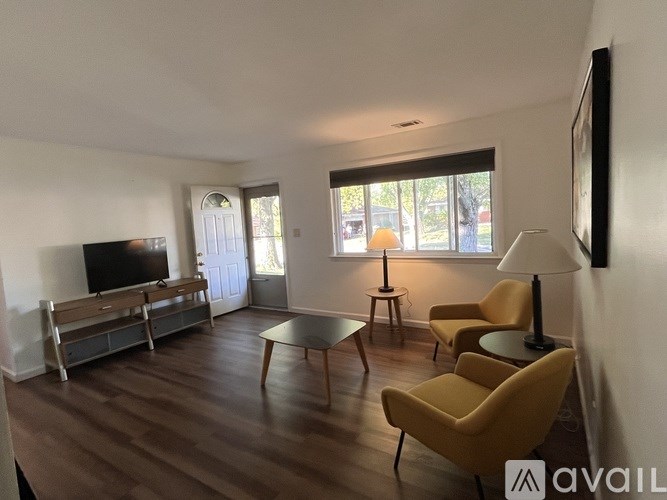 A living room with a television, two chairs, a table, and a window.