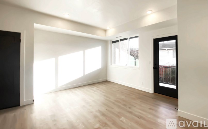 A spacious room with wooden flooring and large windows.