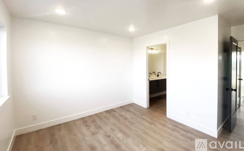 A room with wooden flooring and white walls, with a doorway leading to another room.