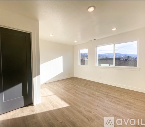 A spacious room with wooden flooring and large windows overlooking a landscape.