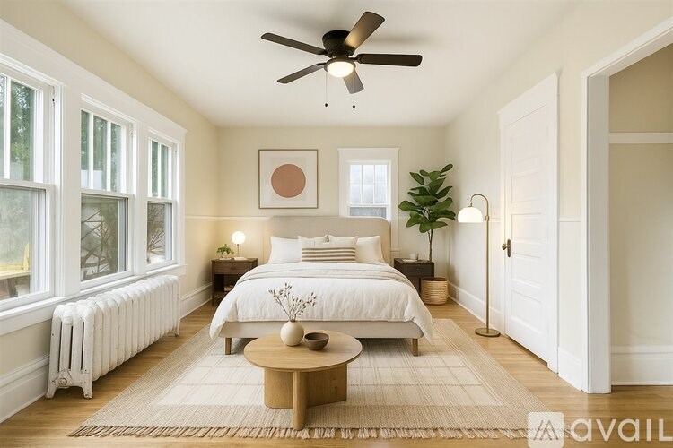 A bedroom with a large bed, a ceiling fan, and a window with a white radiator.