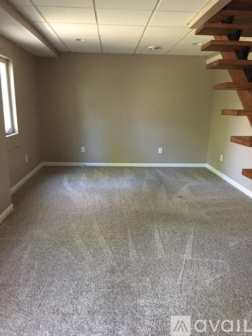 A room with a carpeted floor and a staircase on the right side.