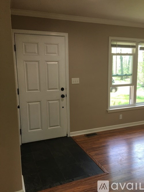 A white door with a black handle is in a room with a brown floor and a window.