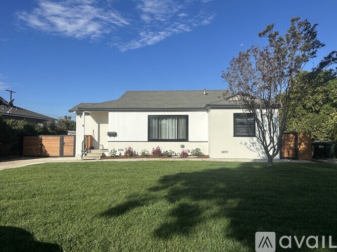 A house with a white exterior and a grey roof is surrounded by a green lawn.