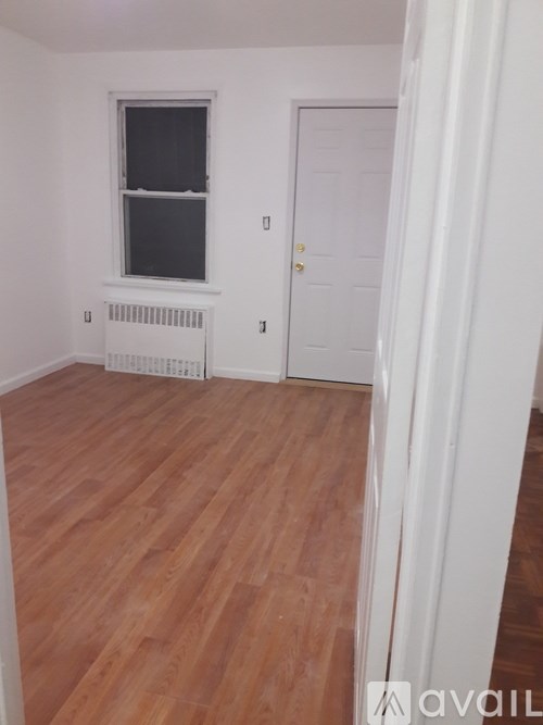 A room with wooden flooring, a white door, and a window with a white frame.
