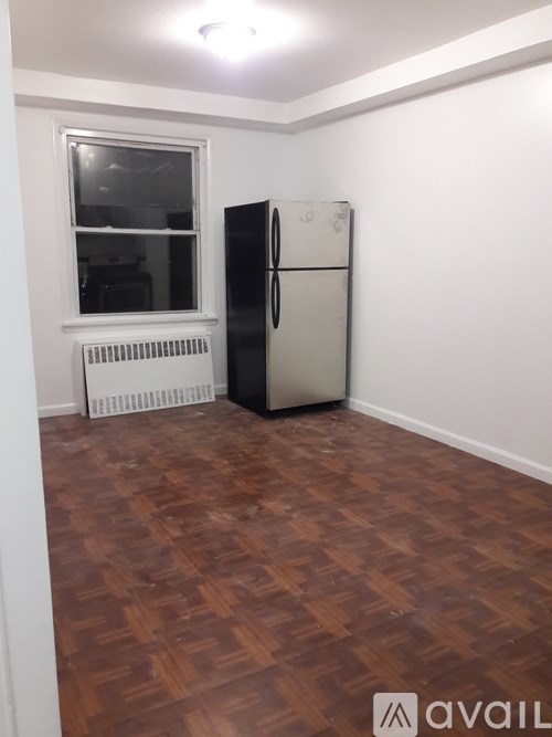 A room with a wooden floor, a window, a radiator, and a fridge.