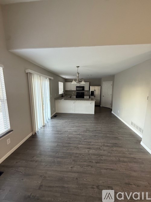 A spacious room with wooden flooring and a chandelier hanging from the ceiling.
