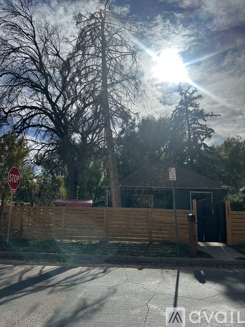 A stop sign is on the left side of a street with a house and trees in the background.