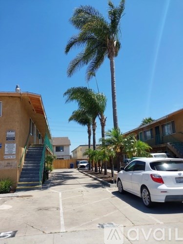 A white car is parked on the side of a street with a building and palm tree in the background.